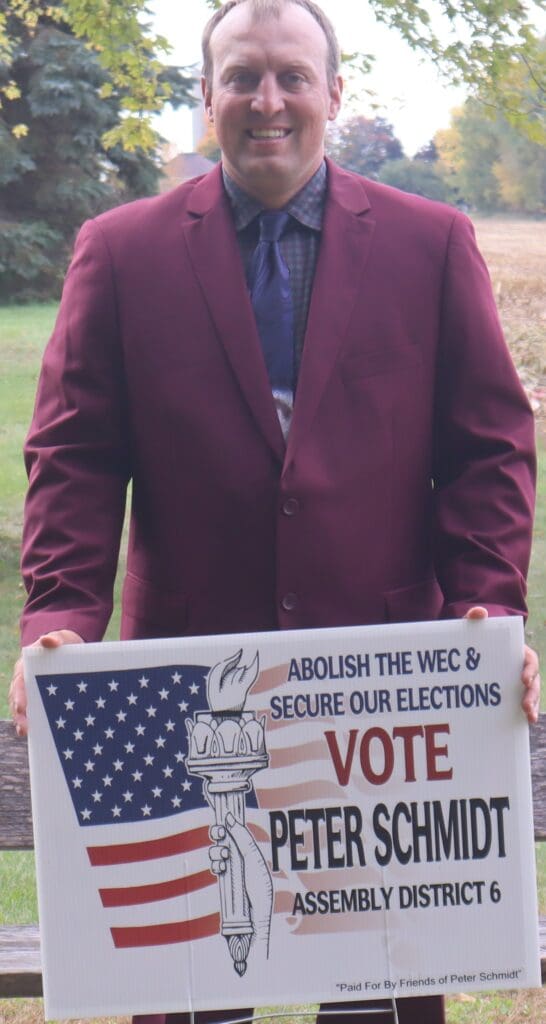 Smiling man in maroon jacket holding campaign sign
